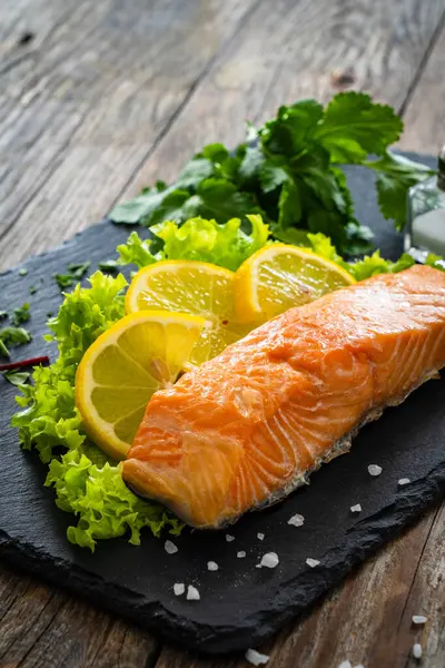 Smoked salmon with lemon and greens on black stony plate on wooden background
