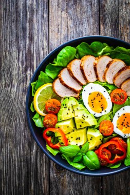 Tasty salad - roasted veal loin, avocado, boiled eggs and fresh vegetables on wooden table  clipart