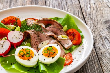 Tasty salad - roasted beef loin boiled eggs and fresh vegetables on wooden table  clipart