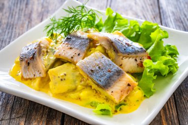 Marinated herring fillets in mustard sauce with dill and lettuce on wooden table  clipart