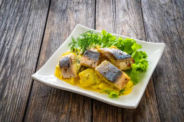 芥末酱中的腌制鲱鱼片 在木制桌子上涂上丁香和生菜 免版税图库图片