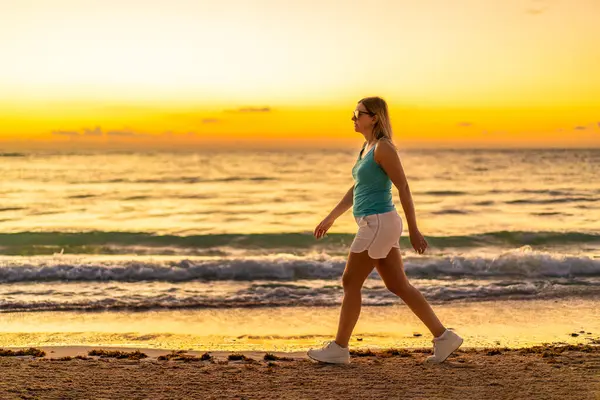 美丽的中年女子在阳光灿烂的海滩上散步 图库图片