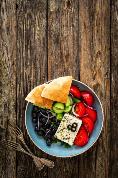 希腊风格的沙拉 新鲜蔬菜 配上意大利芝士 比萨面包和黑橄榄 放在木桌上的碗里 免版税图库照片