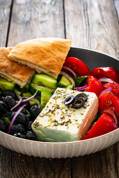 希腊风格的沙拉 新鲜蔬菜 配上意大利芝士 比萨面包和黑橄榄 放在木桌上的碗里 图库照片