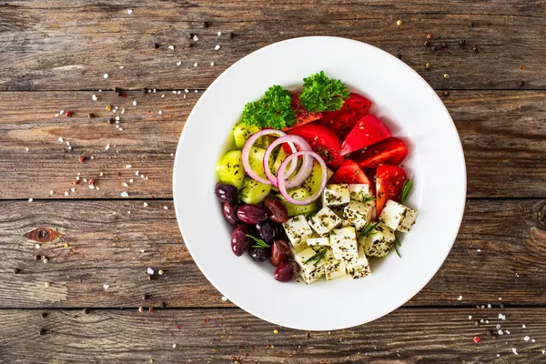 希腊风格的沙拉 新鲜蔬菜 配上意大利芝士和番石榴 放在木制桌子上的白碗里 免版税图库照片