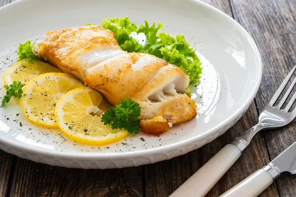 stock image Fried halibut steak, lettuce and sliced lemon on wooden table 