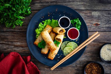 Spring rolls and sauces on wooden table clipart