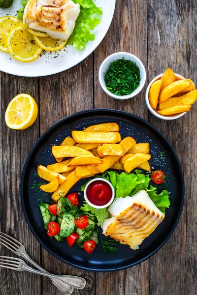 stock image Fried cod loin with fried potatoes and fresh vegetables on wooden table 