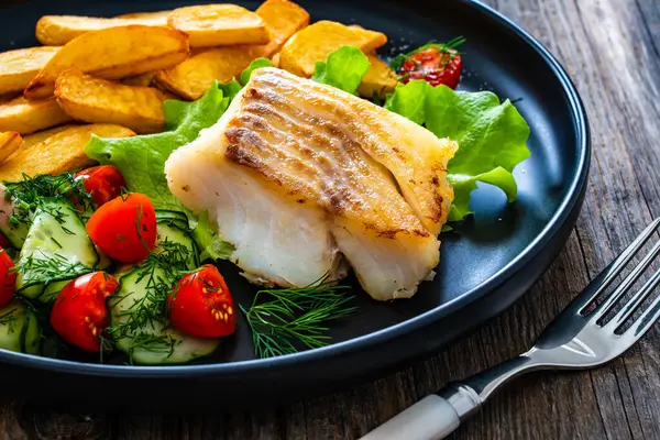 stock image Fried cod loin with fried potatoes and fresh vegetables on wooden table 