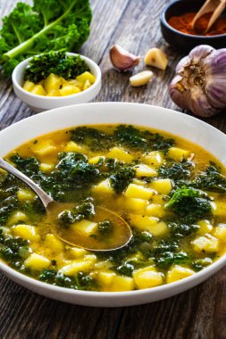 Portuguese green soup - Caldo Verde. Potato and kale soup served in white bowl on wooden table clipart