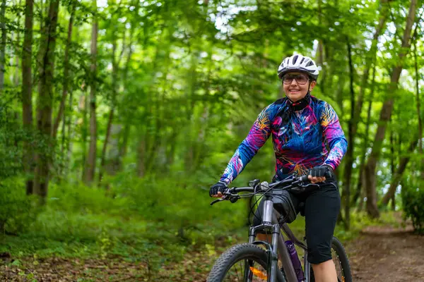 Cycling training in city. Young joyful woman in white helmet and colorful blouse and black shorts riding bike on bike path in city. Playing sports outdoors in spring. Healthy lifestyle