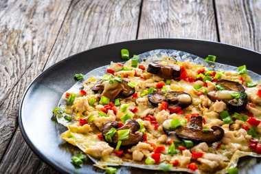 Vietnamese pizza - rice pepper omelet with mushrooms chicken meat and fresh vegetables served on black plate on wooden table  clipart