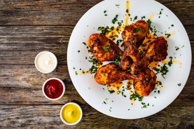 Barbecue chicken drumsticks with French fries on wooden table clipart