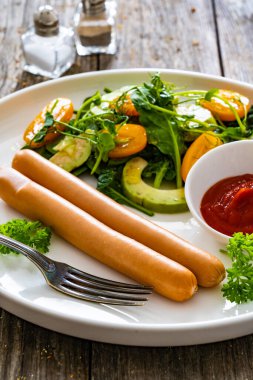 Breakfast - boiled sausages and fresh vegetables served on wooden table clipart