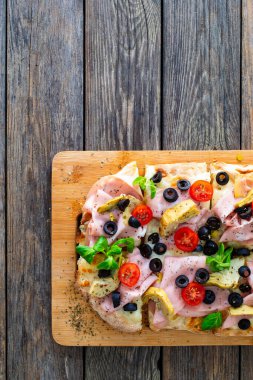 Roman Pizza with mozzarella cheese, boiled ham, cherry tomatoes, black olives and artichokes on wooden table clipart