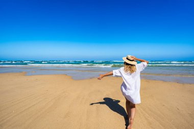 Happy middle-aged woman tourist enjoying sun and beautiful sandy beach on Armona island, Portugal. Back view clipart