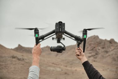 İki adamın elleri dağlarda bir yerde, video kaydında büyük bir insansız hava aracı yakalıyor.