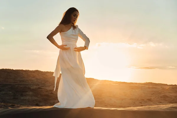 落日的时候 一个穿着苍蝇白色衣服的女孩在沙漠里跳舞和摆姿势 — 图库照片