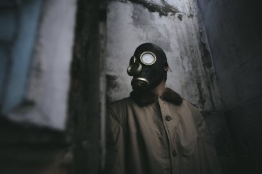 Gaz maskeli bir adam eski bir binanın içinde dikiliyor, köşeyi dönüyor, kitap kapağı için iyi.