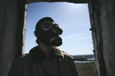 Gaz maskesi takan biri yıkılmış bir evin penceresinin önünde duruyor, kitap kapağı için iyi.