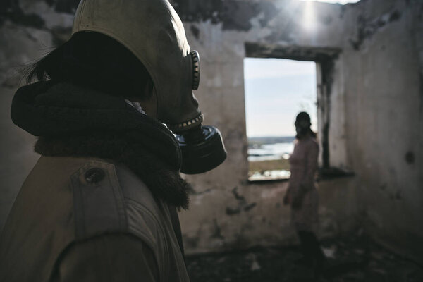 Two people, a guy and a girl in gas masks, stand inside an abandoned house  and look at each other, apocalypse