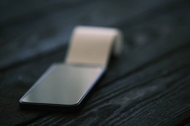 Siyah ahşap masa üzerinde açık çek olan bir cep telefonu, finansal konsept.