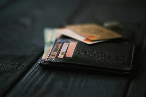 A mobile phone laying on a leather purse and small stack of coins on black wooden table, financial concept