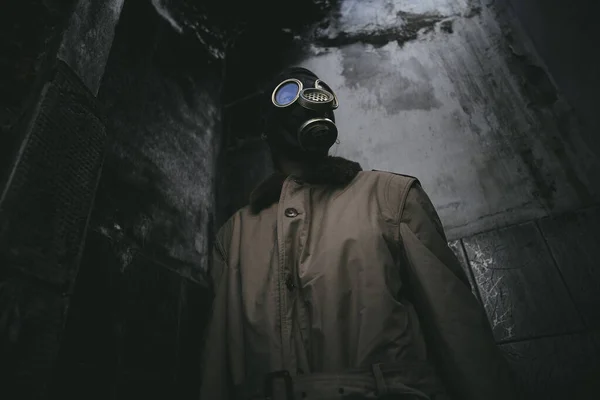 一个戴防毒面具的男人 在一幢破烂不堪的大楼里 他的屋顶在黑暗中漏水 天启了 适合书皮 角度低 — 图库照片