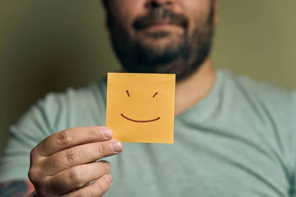 一个满脸胡须的欧洲人在他面前拿着一个橙色的贴纸 脸上带着笑容 图库照片