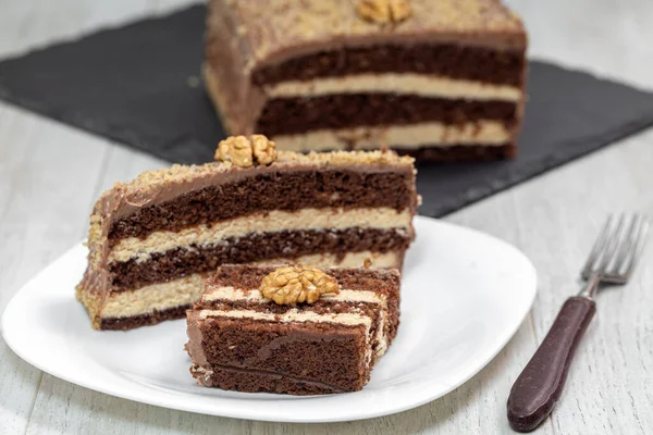 新鲜准备的有核桃的美味巧克力蛋糕 甜甜的坚果甜点 巧克力泡芙蛋糕 一块加坚果的白盘上的奶油蛋糕 免版税图库照片