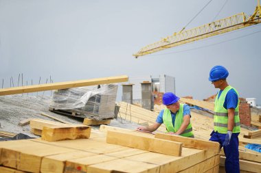Construction workers wearing safety vests and helmets handling wooden planks outdoors