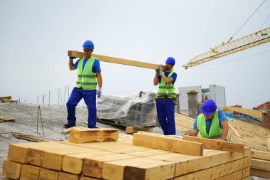 Construction workers carrying wooden beams at building site outdoors