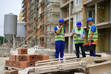 Three construction workers discussing plans at building site outdoors