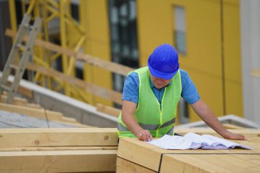 İnşaat işçisi mavi kask takıyor bina planlarını inceliyor.