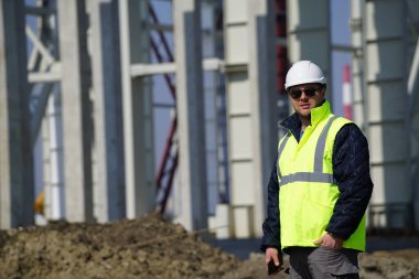 Şantiye iskeletinin yanında duran güvenlik yeleği giyen gülümseyen adam