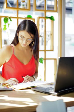 Kameraya gülümseyen dizüstü bilgisayarlı, modern ofiste çalışan gözlüklü mutlu esmer iş kadını. Başarılı Girişimcilik ve Kariyer Konsepti.                            