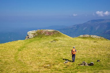 Man hiking across grassy mountain plateau under clear blue sky