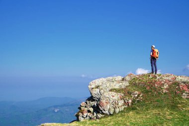 Hiker standing atop rocky cliff overlooking distant blue mountains