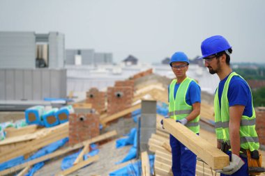 Two construction workers carrying wooden planks at building site outdoors