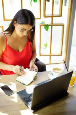 Kameraya gülümseyen dizüstü bilgisayarlı, modern ofiste çalışan gözlüklü mutlu esmer iş kadını. Başarılı Girişimcilik ve Kariyer Konsepti.                            