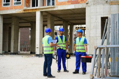 Three construction workers discussing plans outside unfinished building site