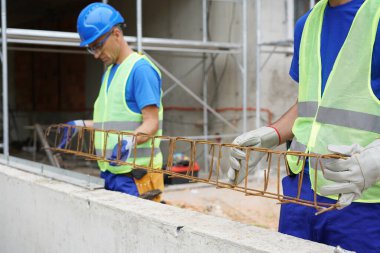 Construction workers wearing safety vests and helmets lifting metal framework outdoors