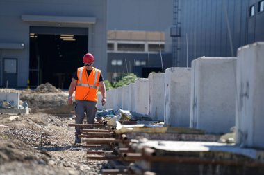 İnşaat işçisi turuncu yelek giyiyor beton bariyerlerin yanında yürüyor