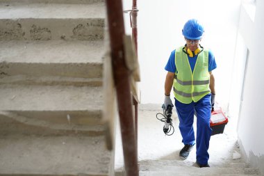 İnşaat işçisi alet çantası taşıyor. Bitmemiş beton merdivenlere tırmanıyor.