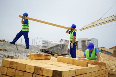 Construction workers carrying wooden beams at building site outdoors