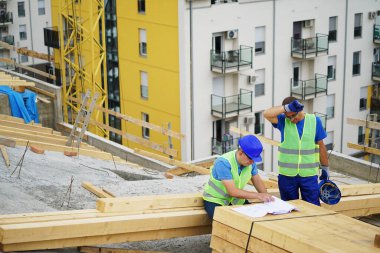 Two construction workers reviewing blueprints at building site outdoors