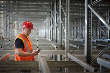 Erkek inşaat işçisi akıllı telefon kullanarak metal iskeleti inceliyor