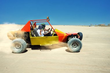 Sarı kumsal arabası mavi gökyüzünün altında kumlu çölde sürüyor.