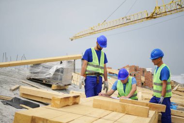 İnşaat alanındaki planları malzemelerle tartışan üç işçi.