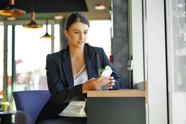 Siyah takım elbiseli şık bir beyaz iş kadını elinde bir cep telefonu ve tabletle elinde müşterilerin iletişime geçmesini bekliyor..